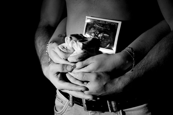 Eltern Hände am Babybauch mit Schühchen und Ultraschallbild